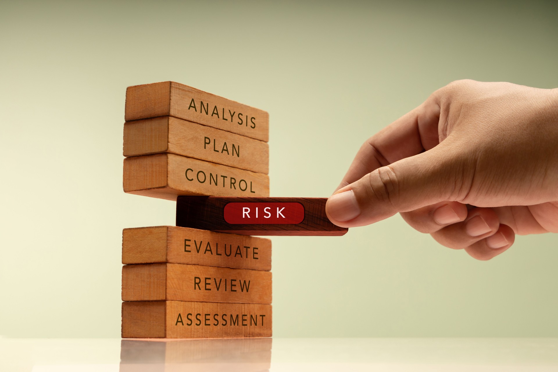 Hand pulls a block labeled RISK from stack of wooden blocks representing structured plans. Core of financial and business risk management